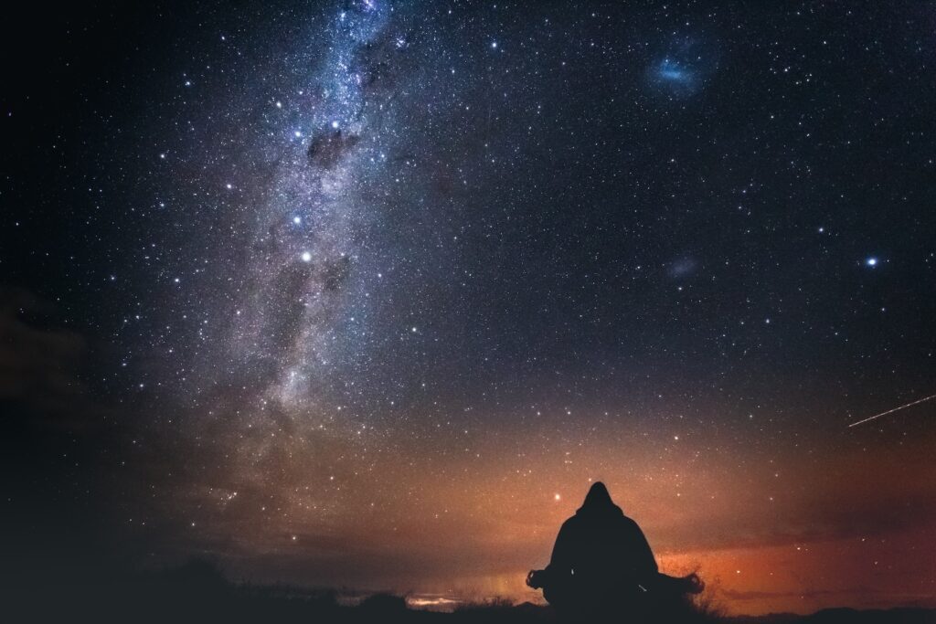 silhouette of person sitting on rock under starry night